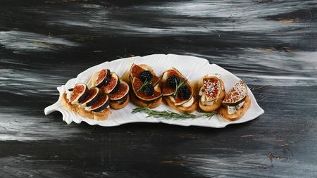 three kinds of bruschettes with figs, cheese, honey on grilled crusty bread on a decorative plate on...