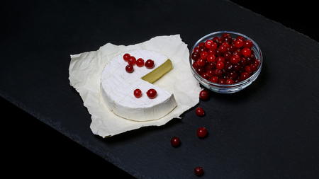 Cheese Camembert or brie and cranberries, with a cut piece, on paper Isolated on a dark stone board, Flat lay. copy space.の写真素材