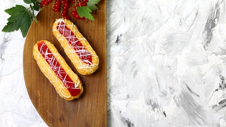 Two Eclairs with Cream Cheese Filling, decorated with red currants jam, on a wooden board. place for text. top view. Authentic lifestyle image.の写真素材