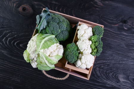 View of organic broccoli and cauliflower in a wooden box, on a black background. Authentic lifestyle image. Seasonal harvest crop local produce concept. top view.の写真素材