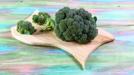 Healthy Green Organic Raw Broccoli Florets Ready for Cooking. Bunch of fresh green broccoli on a wooden board, colored wooden background. top view, place for text.の写真素材