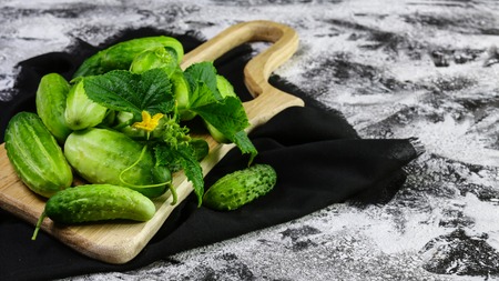 Fresh green cucumber on wooden plate and on dark fabric. Authentic lifestyle image. Top view. Copy space.の写真素材