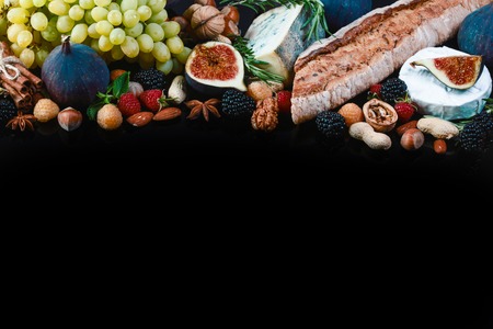 Wine and snack set. Baguette, white, figs, grapes, nuts, cheese variety, meat appetizers and herbs Frame isolated on black background, top view.の写真素材