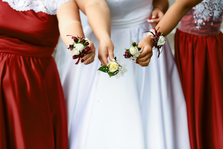 Beautiful wedding boutonier with red and white flowers in the hands of the bride and girlfriends.の写真素材