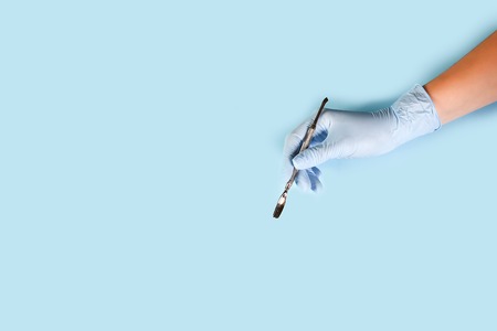 master nails in blue gloves holds manicure tool. set of manicure accessories on blue background top view. Composition for card with a place for text.の写真素材