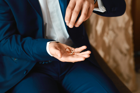 A stylish bridegroom in a dark blue suit suit tosses wedding gold rings from her hands.の写真素材