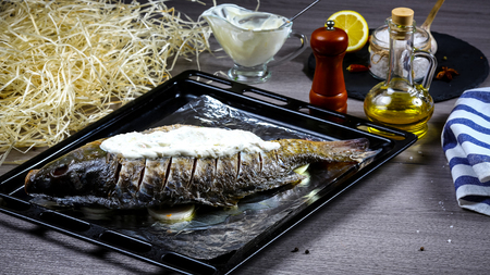 Preparation of fresh fish for baking with vegetables and watered sour cream sauce on an old baking sheet.の写真素材