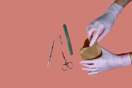 packing a manicure tool in kraft packages before sterilizing in a dry oven. Manicure tool in the hands of the master isolated on pink background. Close up.の写真素材
