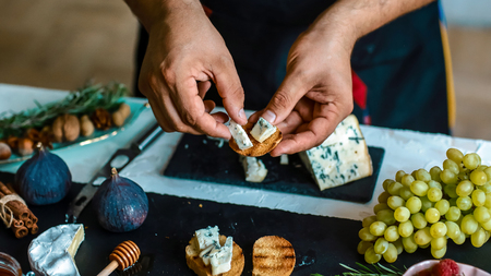 Cooking Bruschettas with figs, Blue cheese and walnuts on grilled crusty bread by chef hands on shale board. Food recipe concept.の写真素材