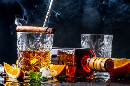 Elite drink for masculine relaxation Two glasses of whiskey, rum and smoking cigar, ice on black background, copy space. concept luxury drink.の写真素材