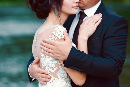 Happy bride and groom after the sunset against the background of a blue evening near blue lake. Wedding dress, wedding details. Groom hugs bride.の写真素材