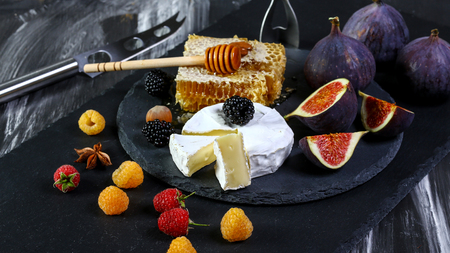 Cheese Camembert with figs, raspberry and blackberries on old black wooden table. Food for wine and romantic, cheese and bread delicatessen. Text area space.の写真素材