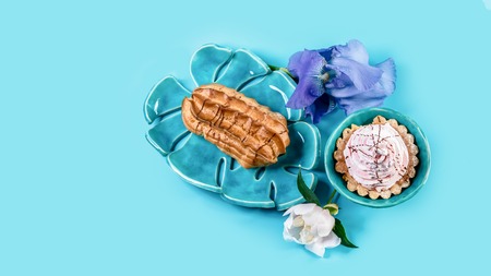 Traditional french eclairs and spring flowers on a blue ceramic plate, isolated on blue background. Top view. Copy space.の写真素材