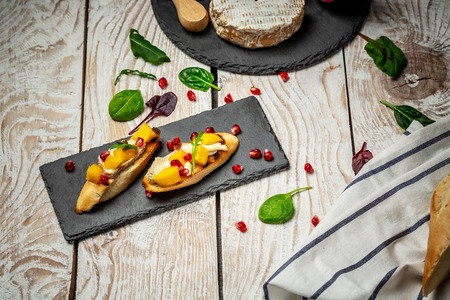Antipasti snacks for Wine. Brushetta with mango, Camembert cheese and pomegranate served on a shale board, rustic wooden table. Top view.の写真素材