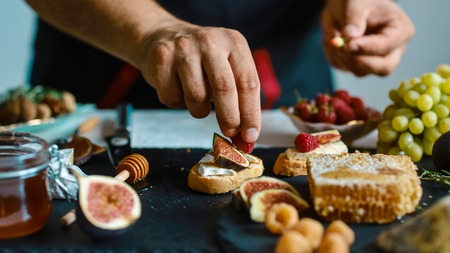 Food recipe concept. Toasts of cheese, figs and honey in hands in the kitchen. This Fig and Gorgonzola tartines, toast, bruschetta. drizzled with honey.の写真素材