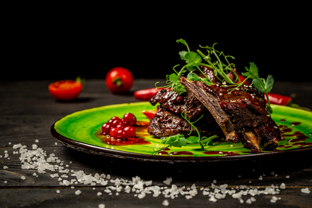 Delicious barbecued ribs seasoned with a spicy berry sauce and served with green seedlings on the plate, old rustic wooden background. Beautiful dish in the restaurant. space for text.の写真素材