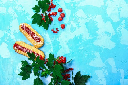 bright eclairs with fruit berry filling with red currant. on blue background, top view. space for...
