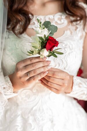Close-up of the bride's hands holds a boutonniere. boutonniere with red rose.Beautiful sensual bride...
