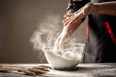 A cook in black knead the dough in a glass bowll bowl for cooking bread in the kitchen. Yeast dough made with loveの写真素材