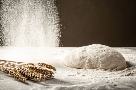 Cooking bread. The dough lies on a wooden kitchen table and sprinkled with flour on top. Isolated on dark background. Empty space for text.の写真素材