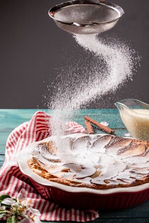 Traditional English cuisine. Powdered sugar is poured out of a sieve on a cheesecake. cheese cake with apples and vanilla cream.の写真素材