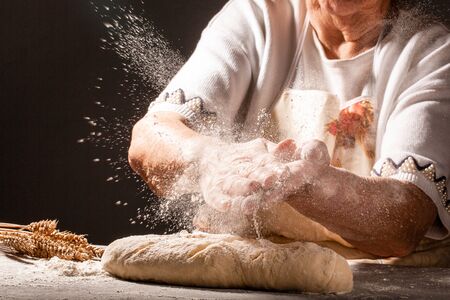 Photo of flour and old woman, grandmother hands with flour splash. Cooking bread. Kneading the Dough. Isolated on dark background. Empty space for text.の写真素材