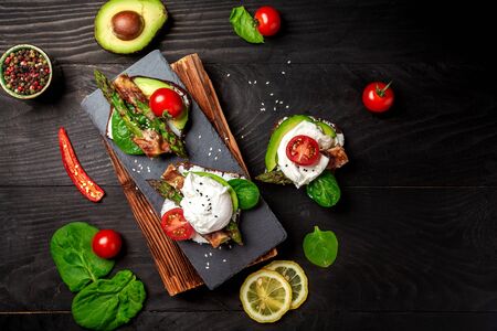 Italian food: snack toasts with avocado, asparagus and fried egg, top view. Food recipe background.