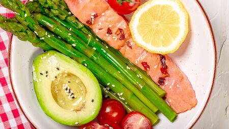 Baked salmon garnished with asparagus and tomatoes with avocado. Top view. Food recipe background....