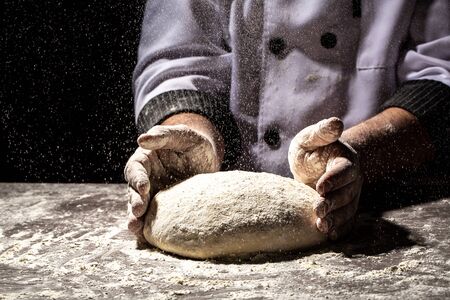 Beautiful and men's hands knead the dough from which they will then make bread, pasta or pizza. A cloud of flour flies around like dust. Food conceptの写真素材