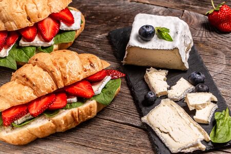 Breakfast, business lunch, sandwiches Croissant with strawberries and soft cheese with mold brie camembert on wooden background. banner menu recipe top view.の写真素材