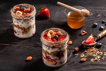 Healthy blueberry and strawberry parfait in a mason jar on a dark background. granola, berries, nuts and yogurt.の写真素材