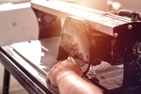 Worker hand cutting ceramic tile with water cutting machine close-up. Circular saw for tile...