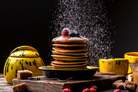 Stack of pancakes with sugar powder splashes on wooden dark background table. Copy space for your text.の写真素材