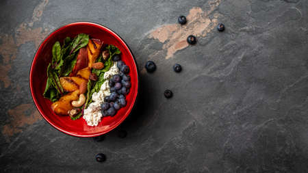 Kale salad with caramelized peaches, blueberry and goat cheese, wooden background. Long banner format, top view.の写真素材