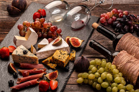 still life, food composition with assorted cheese, glass of wine and fruits on a wooden table.の写真素材