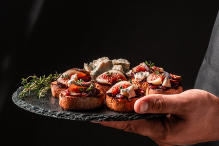 Canape or crostini with toasted baguette, blue cheese, onion jam, figs and fresh thyme on a slate board in the hands of the chef, Food recipe background. space for text.の写真素材