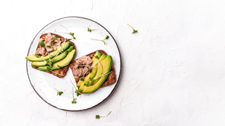 Sandwiches with avocado and tuna fish, microgreen, wholemeal bread. Delicious breakfast or snack on a light background, top view. Long banner formatの写真素材
