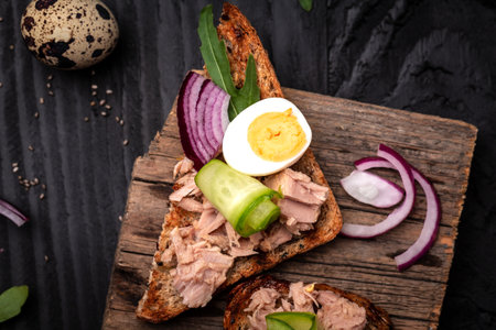 Toasts with tuna. bruschetta sandwiches with wholemeal bread, canned tuna fish, quail eggs and onions, cucumber. Delicious Italian antipasti crostini on wooden boardの写真素材