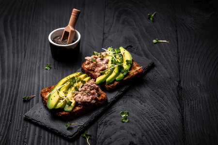 Tuna sandwiches with avocado and microgreen on wholemeal bread, wooden background. Tasty tuna...