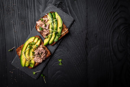 Appetizer bruschetta avocado and tuna fish, microgreen. Toasts with tuna delicious healthy food on a dark background, Top view, flat layの写真素材