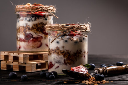 homemade yogurt parfait with granola and blueberries strawberry in glass jar on rustic wooden table. healthy breakfast.の写真素材