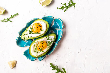 Fried eggs in avocado with fresh herbs and spices. Avocado stuffed with eggs. Delicious breakfast or snack on a light background, top view.の写真素材
