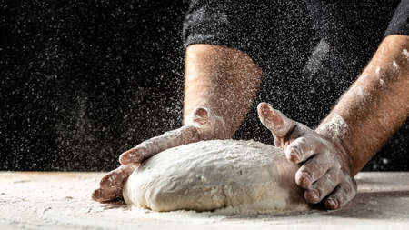 chef in a professional kitchen prepares the dough with flour, Beautiful and strong mens hands knead the dough from which they will then make bread, pasta or pizzaの写真素材