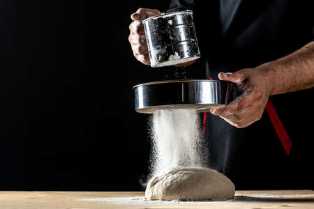 chef in a professional kitchen prepares the dough with flour, Beautiful and strong mens hands knead the dough from which they will then make bread, pasta or pizzaの写真素材