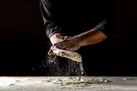 male hands making dough for pizza. Pizza dough. Cooking bread. Kneading the Dough. Isolated on dark background. space for textの写真素材