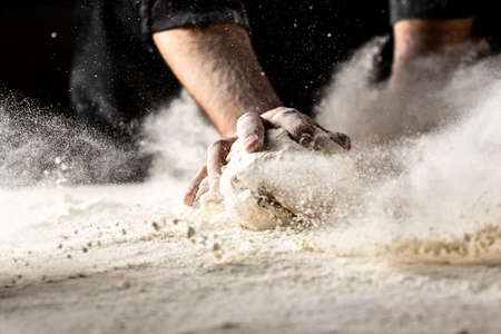 Powdery flour flying into air. chef hands with flour in a freeze motion of a cloud of flour midair. Hands kneading raw dough. Culinary, cooking, bakery conceptの写真素材