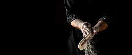 Beautiful and strong mens hands knead the dough make bread, pasta or pizza. Powdery flour flying into air. chef hands with flour in a freeze motion of a cloud of flour midairの写真素材