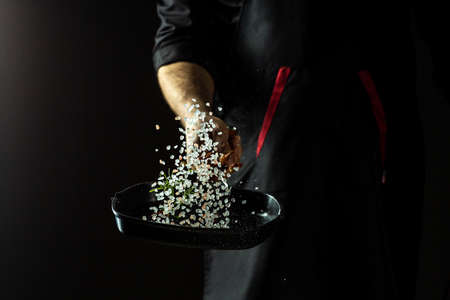 Chef in restaurant cooking food frying aromatic salt with rosemary, dried pepper chili in pan on dark background copy spaceの写真素材