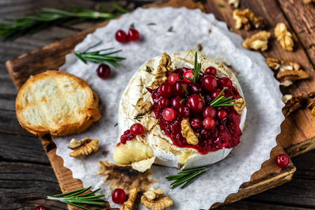 Baked camembert with cranberry sauce, baguette bread and rosemary on rustic wooden table.の写真素材