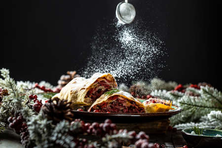 winter dessert strudel with cherry, cranberries and walnut, Christmas decorated with powdered sugar, freeze motion.の写真素材